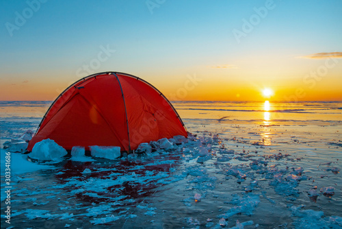 Morning dawn, orange tent stands on the transparent ice of lake Baikal in Russia
