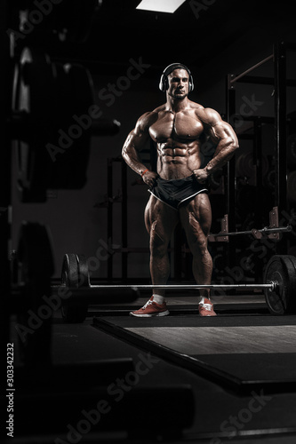 Muscular athletic bodybuilder fitness model training and posing with barbell in gym. Concept sport photo of exercises in gym