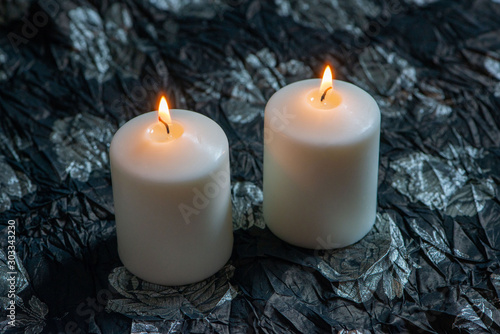 Two lit white candles on dark background.