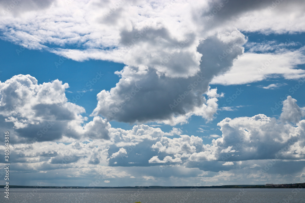 Cumulus and ragged cirrus clouds on a blue sky above the lake. Natural summer background with copy space