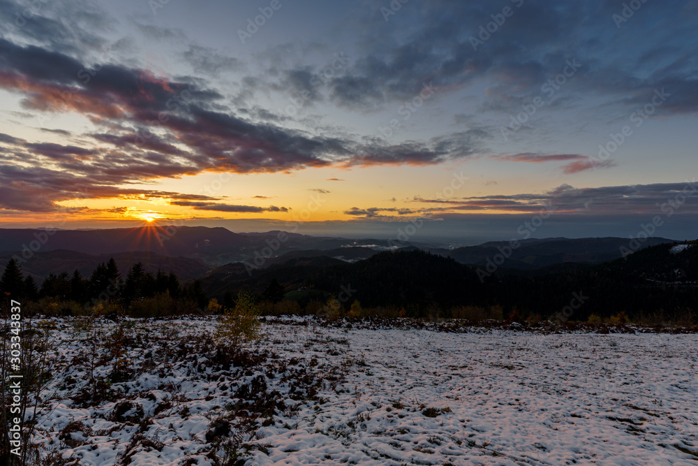 Sunset panorama in the Black Forest Mountains at golden hour with some fog and cloudy sky	
