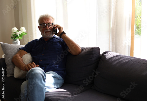 Senior man sitting alone in home and talking friend on smart phone.
