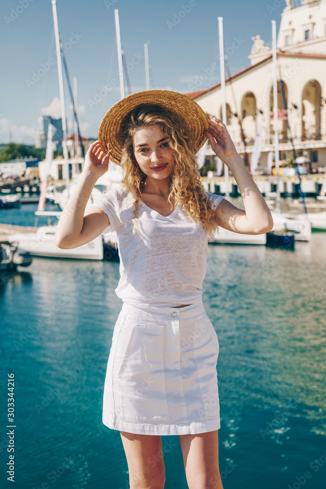 blonde in a straw hat on the background of yachts, the sea and the station building