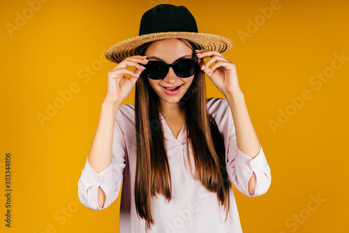 Girl with facial expression "Aha!" takes off black glasses in studio yellow