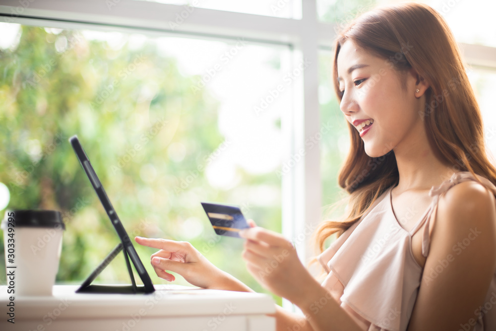 Happy Asian young woman doing online shopping at home.She holding credit card and using laptop computer.Smiling asian woman on couch using tablet to shop online n the living room.