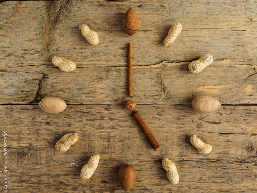 Clock made of different nuts and cinnamon on wooden background. The clock strikes five. Hours of proper nutrition