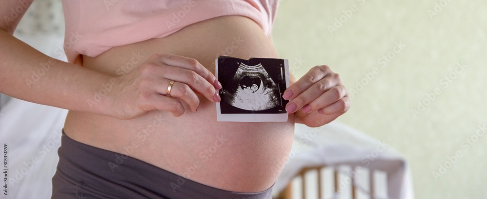 Φωτογραφία Big pregnant tummy and woman's hands holding ultrasound image of healthy unborn baby