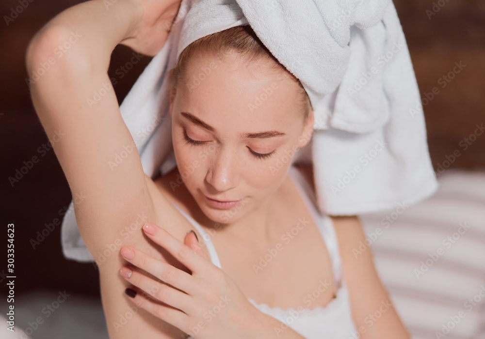 Close view of pretty romantic woman with natural beauty checking armpit after epilation procedure, having wet hair wrapped into soft white towel, examining underarm