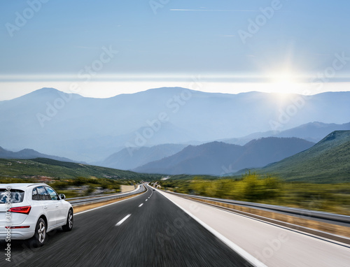White car moves on the road among the mountains and forests.