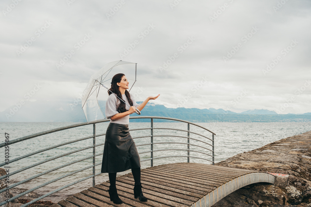 Outdoor portrait of young woman under the rain, holding umbrella, fashion styled image