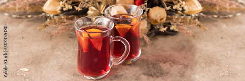 Two glasses of christmas mulled wine with oranges and spices on a textural background. Selective focus. Copy space. Banner.