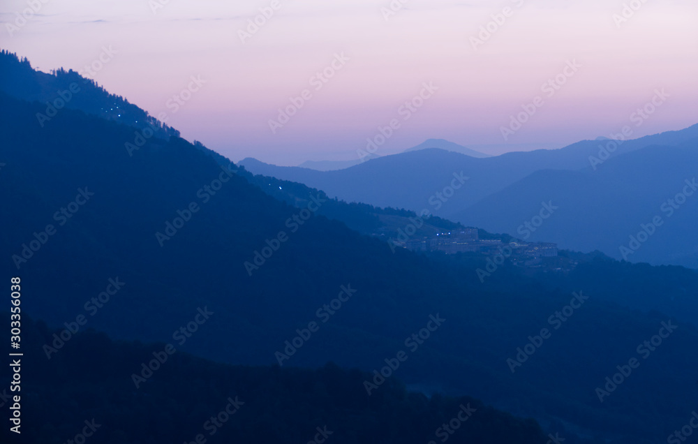 Evening blue mountains. The sun is setting. In the distant city lights. Sochi, Russia.
