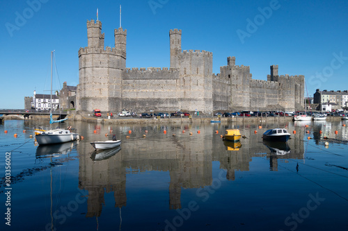 Caernarfon Castle Overlooks the river Seiont flowing past the old town of Caernarfon where locals have moored their boats with the castle reflected in the high tide of the water. photo