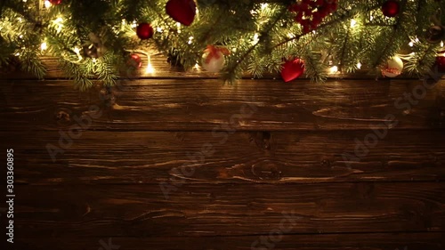 Blurred Christmas background, with fir branches, fairy lights and christmas decorations on brown wooden plank