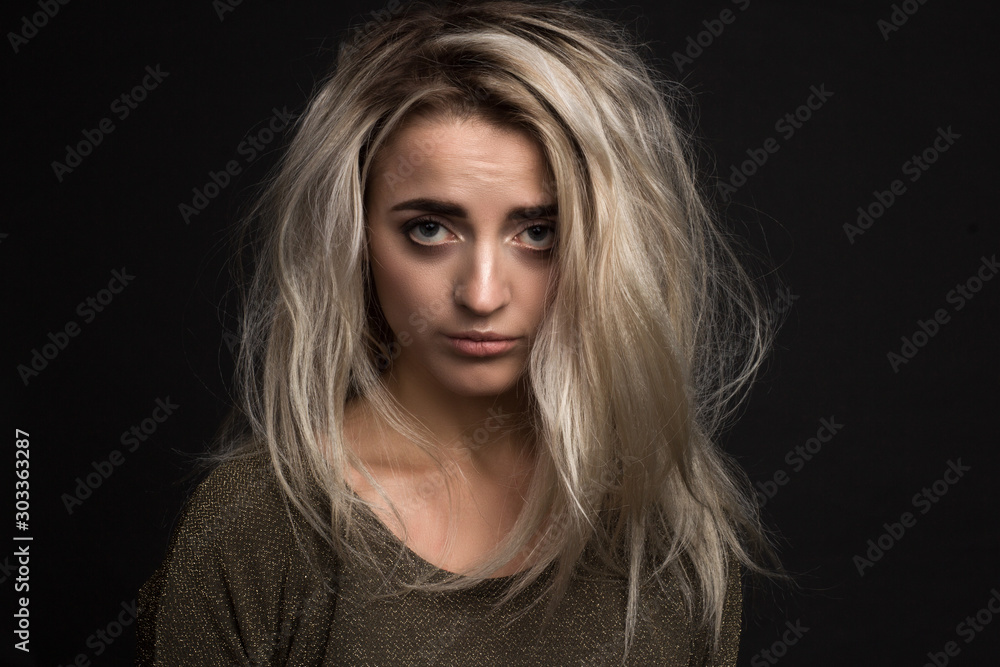 portrait of a young beautiful girl with an offended expression and disheveled hair on a black background
