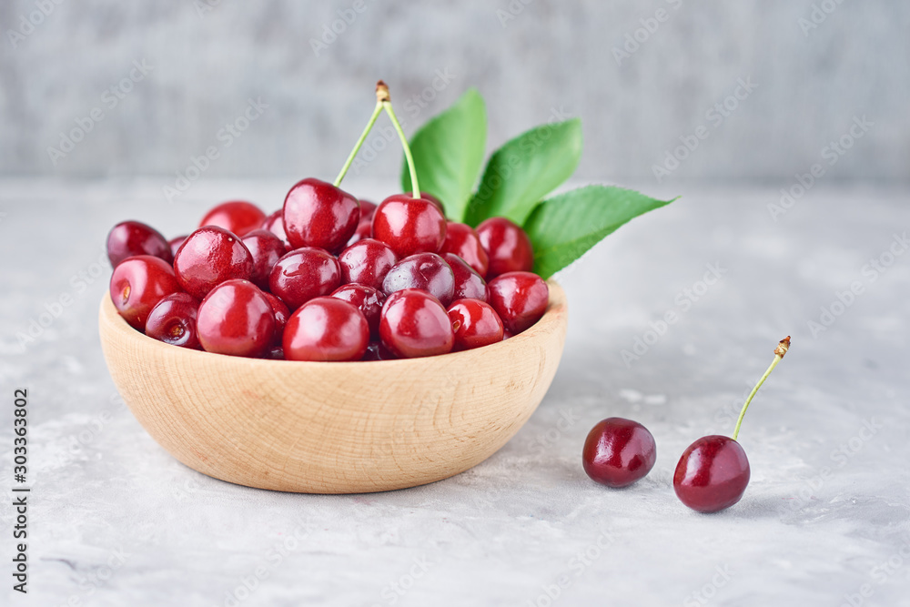 Red fresh cherry beries in wooden bowl on a gray background Red fresh cherry beries in wooden bowl on a gray background