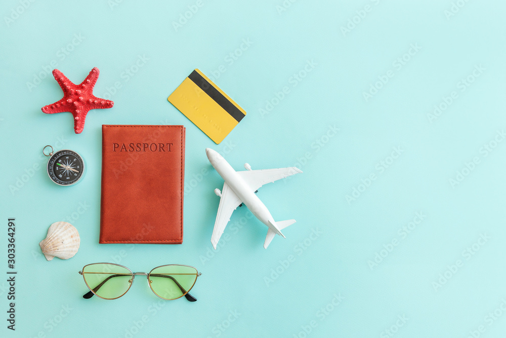 Vacation travel adventure trip concept. Minimal simple flat lay with plane passport sunglasses compass gold credit card shell on blue pastel colourful trendy background. Tourist essentials - obrazy, fototapety, plakaty 