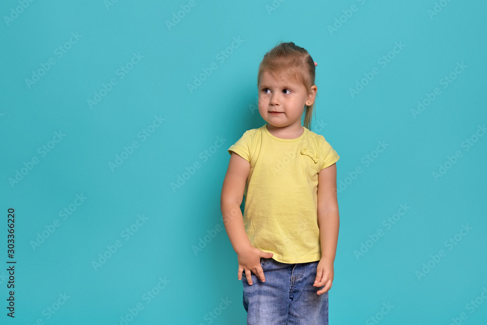 Close-up studio shot of a beautiful little girl. Little blonde girl in a yellow T-shirt on a blue background. The emotions of a child.