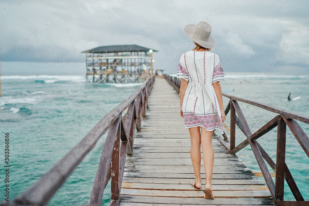 Vacation on tropical island.  Back view of young woman in hat enjoying sea view from wooden bridge terrace, Siargao Philippines