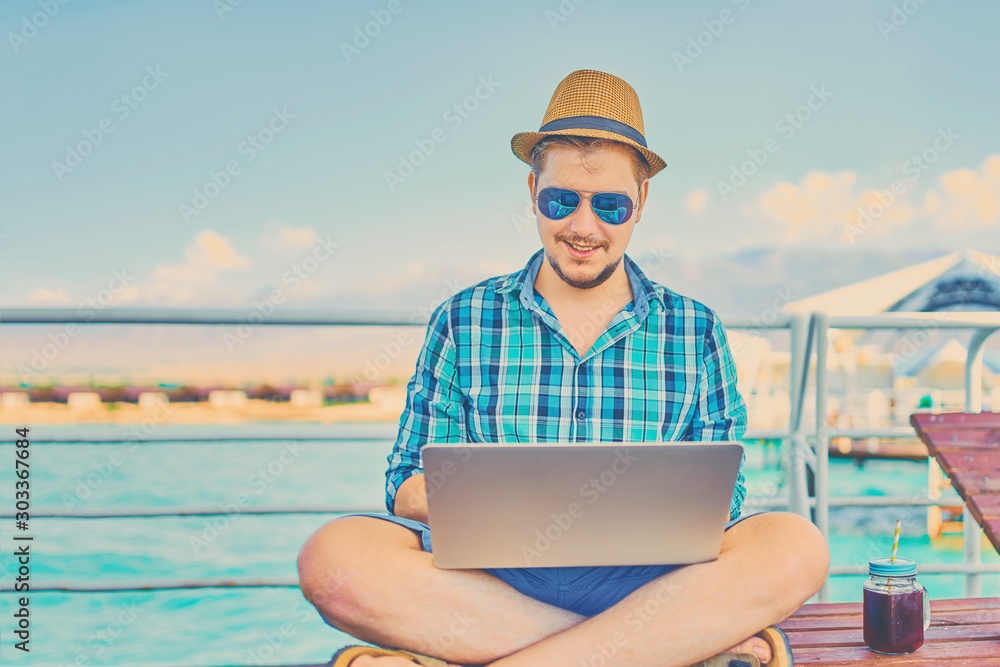 A man on vacation, sits on the pier and works.