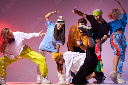 Hip hop battle in spacious dance hall, young people dancing break dance, pretty sportive girl in white hoodie and black loose pants showing street dance movie
