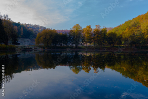 Fresh water lake in a former quarry with reflections of the Indian summer and autumn colors of the leaves on an early morning in November
