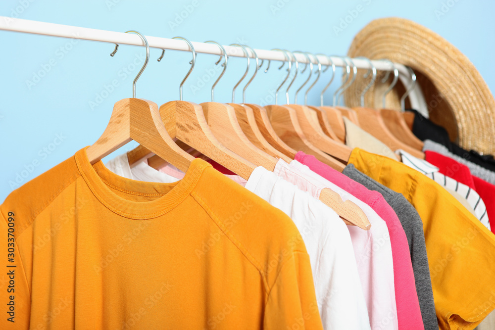 Fototapeta premium fashionable clothes on hangers on a wardrobe rack on a colored background.
