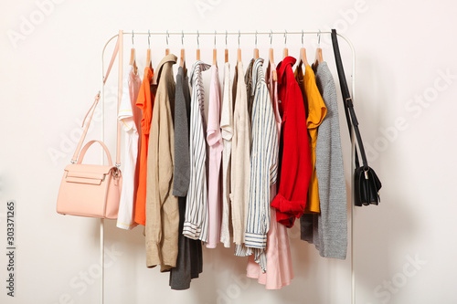 Fashionable clothes on hangers on a wardrobe rack on a light background.