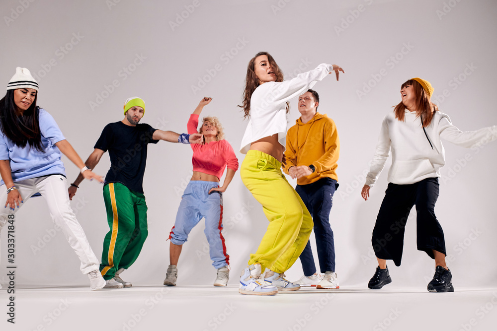 group of happy young people dancing cheerfully on stage of dance school studio, female professional trainer showing hip hop movie, break dancers preparing for festival, side shot
