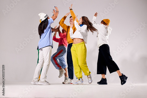 Cheerful friends clapping hands in the air, gathered together, expressing happiness, celebrating winning of gold, playfully jumping, congratulating each others, hip hop dance competition