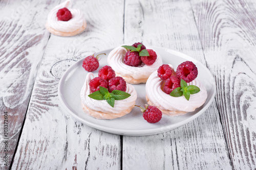 Mini Pavlova cakes topped with raspberries and mint on white wooden table