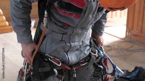industrial climber puts on equipment for high-altitude work. on climber s belt carabiners.