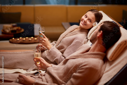 Spa, relax, enjoying concept. Married couple together relaxing in spa salon, lying on beds drinking champagne, using candles