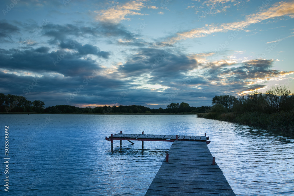 Wooden plank bridge, calm lake and evening clouds on the sky
