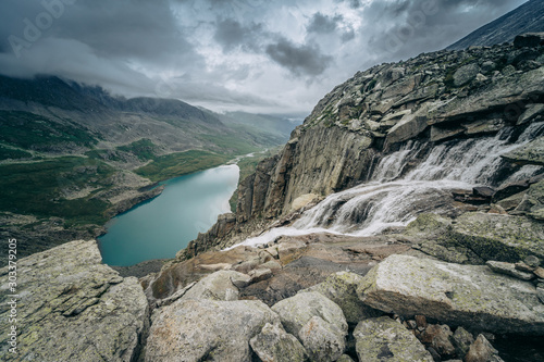 Wild russian nature. Beautiful landscape with emerald lake and waterfall in the mountains. Clear turquoise water. Traveling in the Altai Republic. Tourism in Russia. Dramatic sky over Akchan Lake. photo