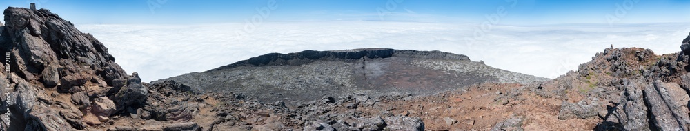 Large panoramic view of the pit crater at the top of the stratovolcano Mt Pico, Azores, taken from its pinnacle. At 2351m, the summit is the highest point of Portugal. Blue sky is above the clouds. Large panoramic view of the pit crater at the top of the stratovolcano Mt Pico, Azores, taken from its pinnacle. At 2351m, the summit is the highest point of Portugal. Blue sky is above the clouds.