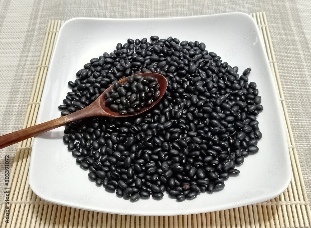 Black beans and wooden spoon in a white plate. Black beans and wooden spoon in a white plate.