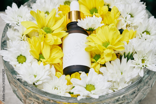 Bottle with moisturizing serum in crystal box with white and ywllow daisy flowers photo