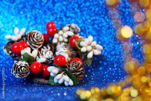 New Year decoration - berries and branches of holly as well as snowy Christmas tree cones on a sparkling blue background. Shallow depth of field. Selective and soft focus