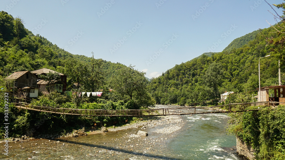 Old residential building by the river and a wooden bridge in mountain georgian at rural fall landscape