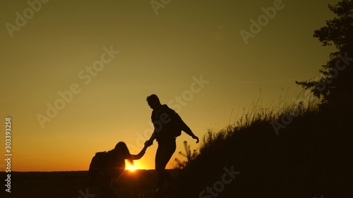 male traveler holds the hand of a female traveler helping to climb top of the hill. Tourists climb the mountain at sunset  holding hands. team work of business partners. Happy family on vacation.