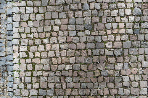 European granite cobblestone pavement with different stones. Gray stone background, textured pedestrian pavement, road.