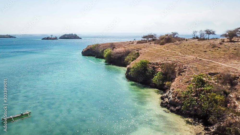 Beautiful headland formations on Lombok, Indonesia. Boats parked on the shores on the Pink Beach, Crystal clear water, shimmering with shades of blue. Drone areal capture. Hidden, unspoiled gem.
