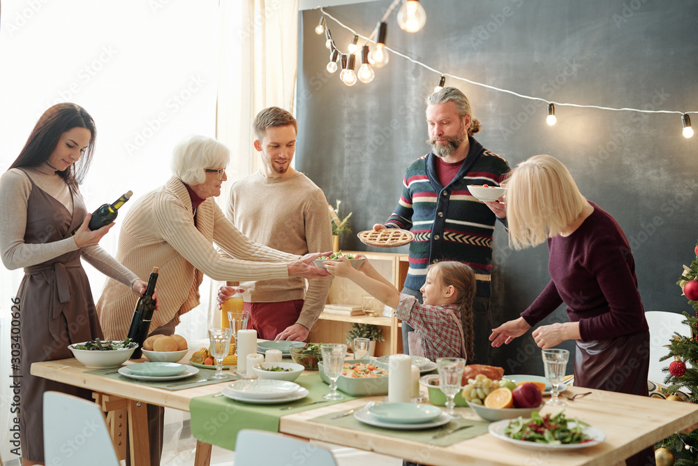 Cute little girl passing bowl with salad to her great grandma by festive table Cute little girl passing bowl with salad to her great grandma by festive table