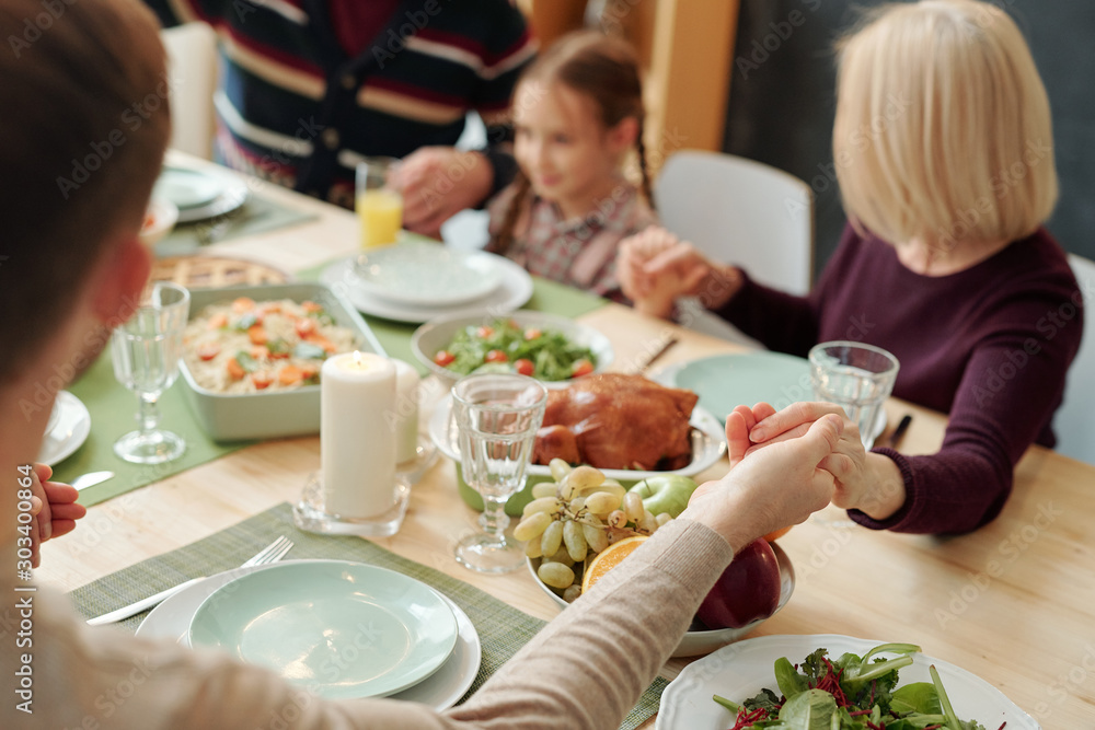 Hands of family held by each other over served festive table during pray Hands of family held by each other over served festive table during pray