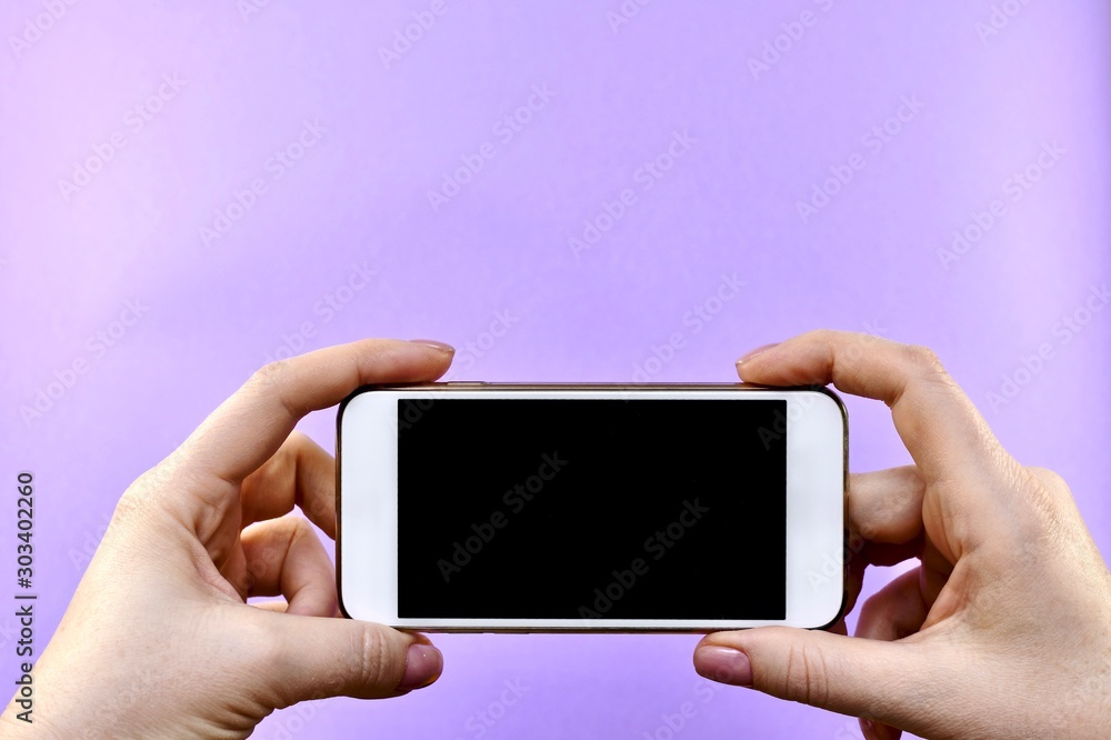 Mobile phone, smartphone with a black screen off in both hands, holding from the right and left. Horizontally centered, down, on a purple background with free space. Mobile phone, smartphone with a black screen off in both hands, holding from the right and left. Horizontally centered, down, on a purple background with free space.