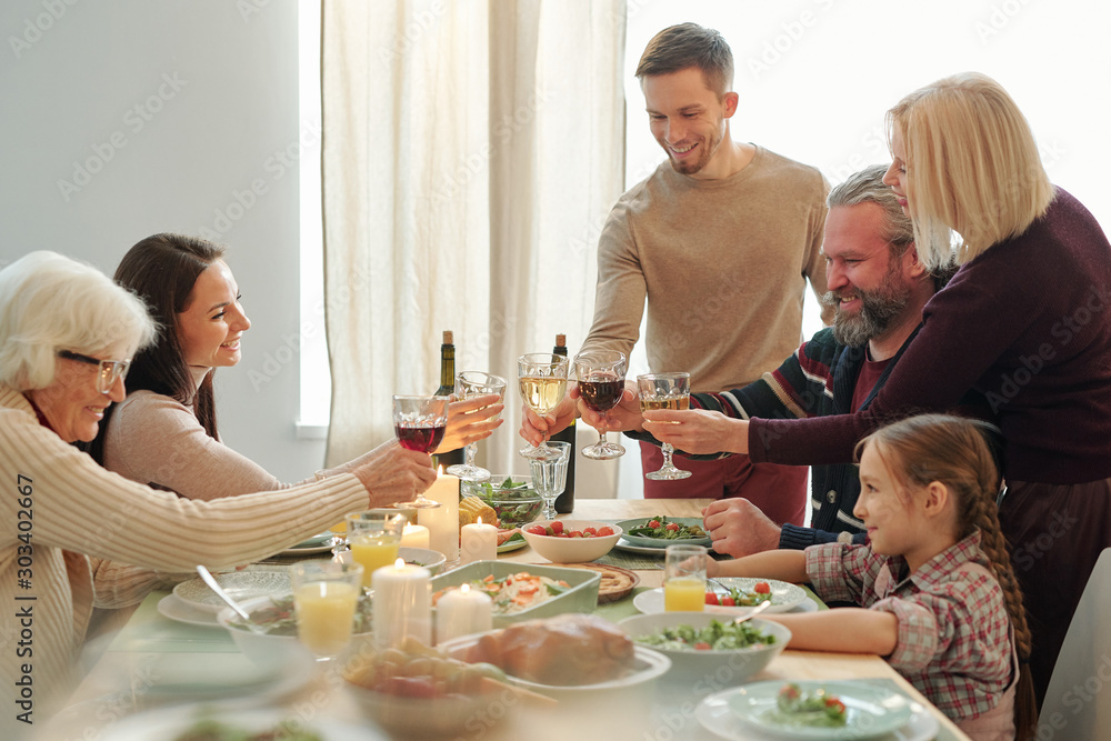 Happy mature and young family members clinking with wine during Christmas toast Happy mature and young family members clinking with wine during Christmas toast