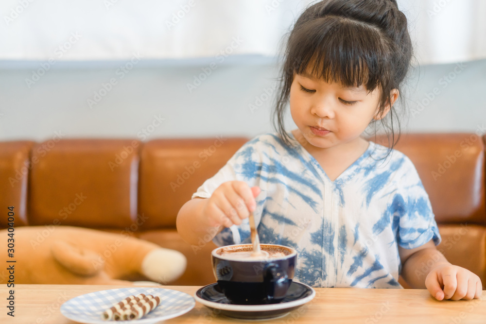 Little Asian girl drinking hot chocolate from cup in restaurant.Enjoy eating and Delicious concept. Little Asian girl drinking hot chocolate from cup in restaurant.Enjoy eating and Delicious concept.