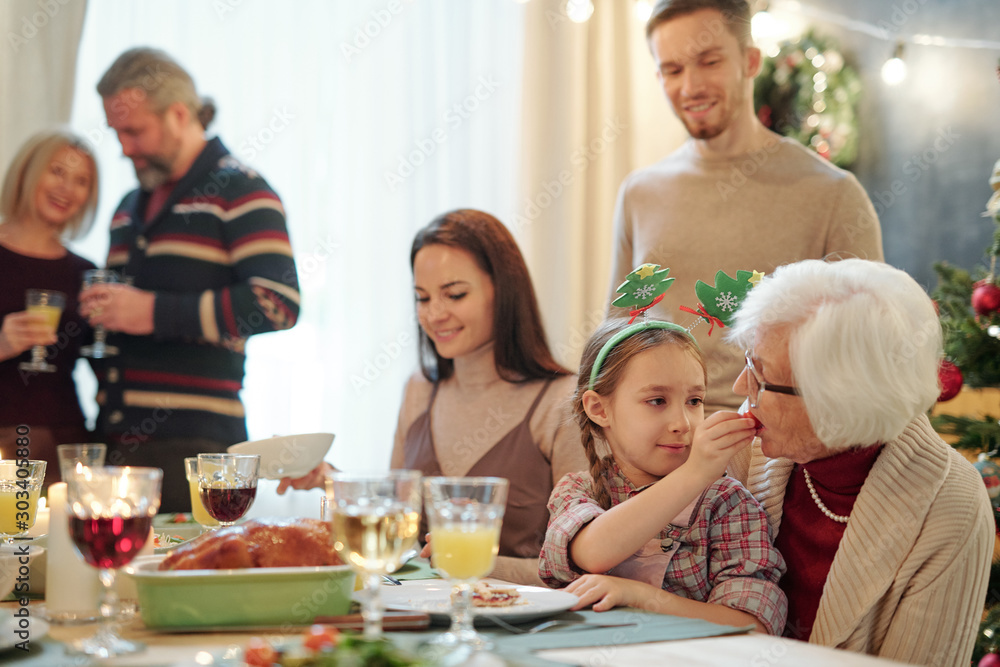Adorable girl giving her great grandmother small tomato by festive table Adorable girl giving her great grandmother small tomato by festive table
