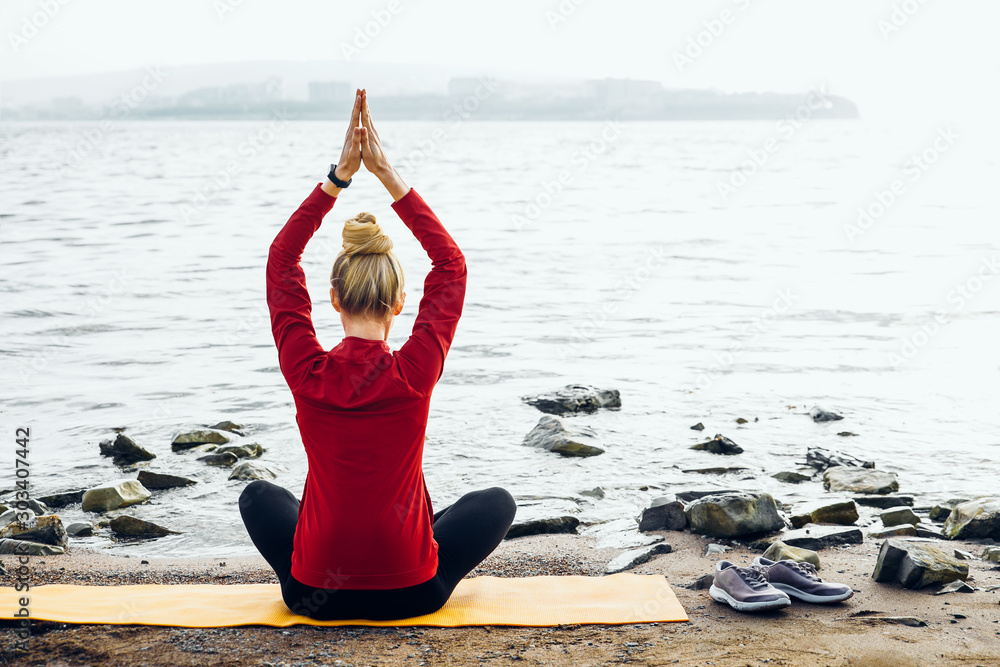 Φωτογραφία Young girl practices yoga in parvatasana lotus position position on seashore background, rear view
